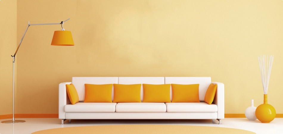 White sofa with orange cushions against a bright yellow wall, with a tall orange floor lamp on the left and yellow decor on the right.